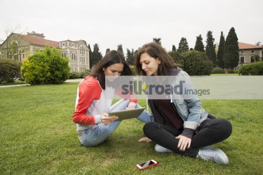 Two friends sitting using device|
