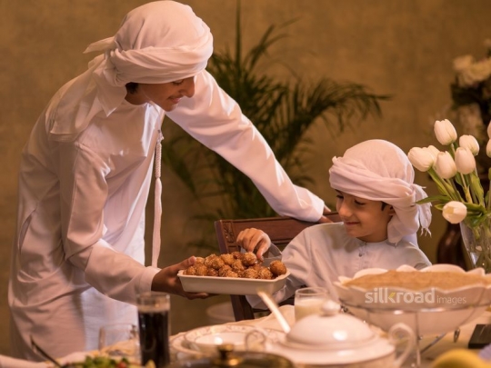 Boy serving brother Arabic sweets|-