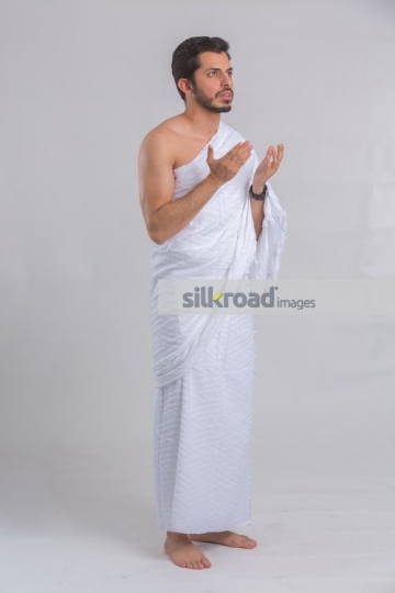 Arab man dressed in the white religious attire praying|